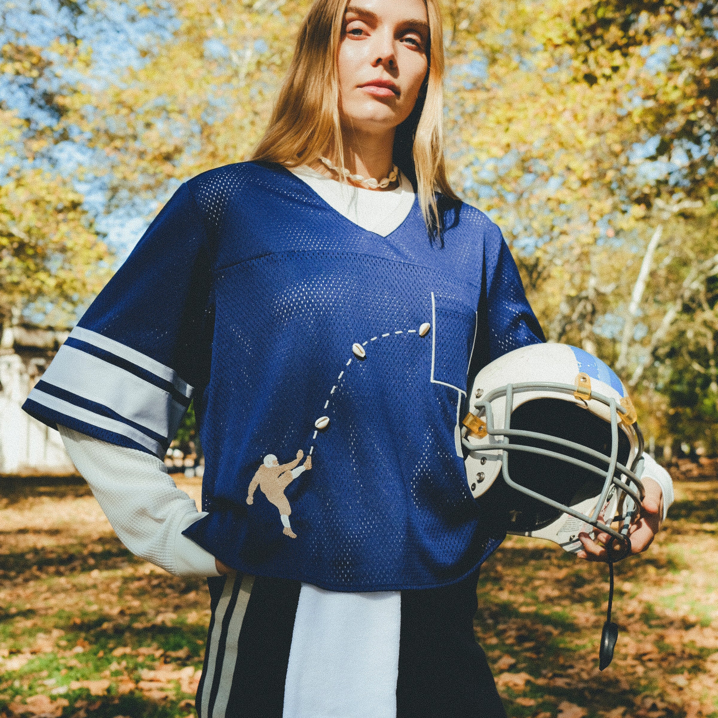 Woman wearing blue mesh jersey, and carrying a football helmet in her arm. 