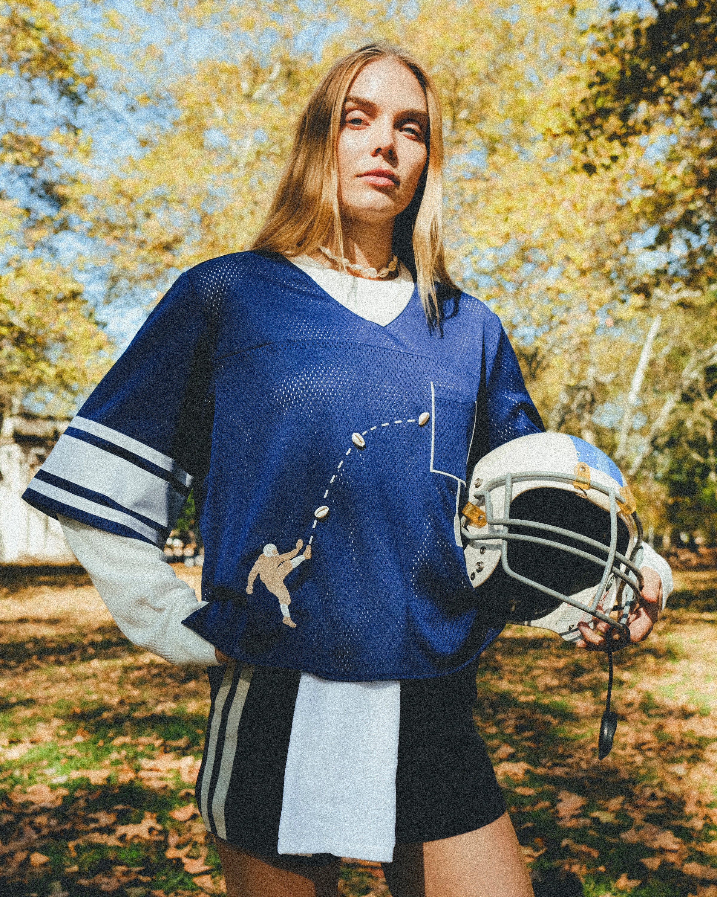 Woman wearing blue mesh jersey, and carrying a football helmet in her arm. 