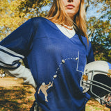 Woman wearing blue mesh jersey, and carrying a football helmet in her arm. 