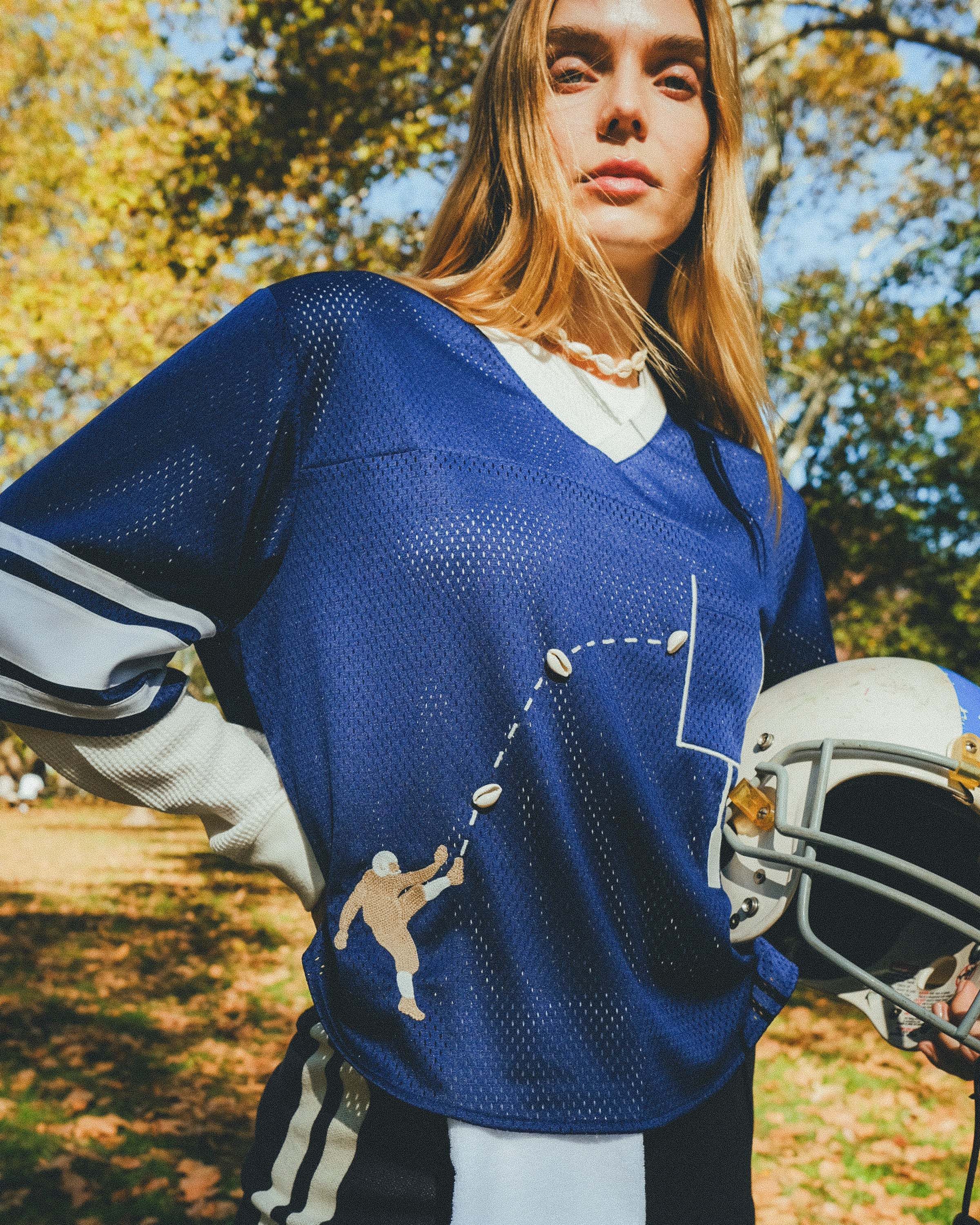 Woman wearing blue mesh jersey, and carrying a football helmet in her arm. 