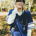 Woman wearing the navy blue mesh football jersey over a white long sleeve shirt. She is laughing and wearing a football helmet. 