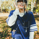 Woman wearing the navy blue mesh football jersey over a white long sleeve shirt. She is laughing and wearing a football helmet. 