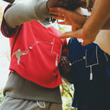 Two people wearing red and navy mesh football-style tops with cowrie shell football graphics, joining hands in a team huddle.