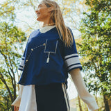Woman wearing blue football mesh jersey crop and smiling off to her right.
