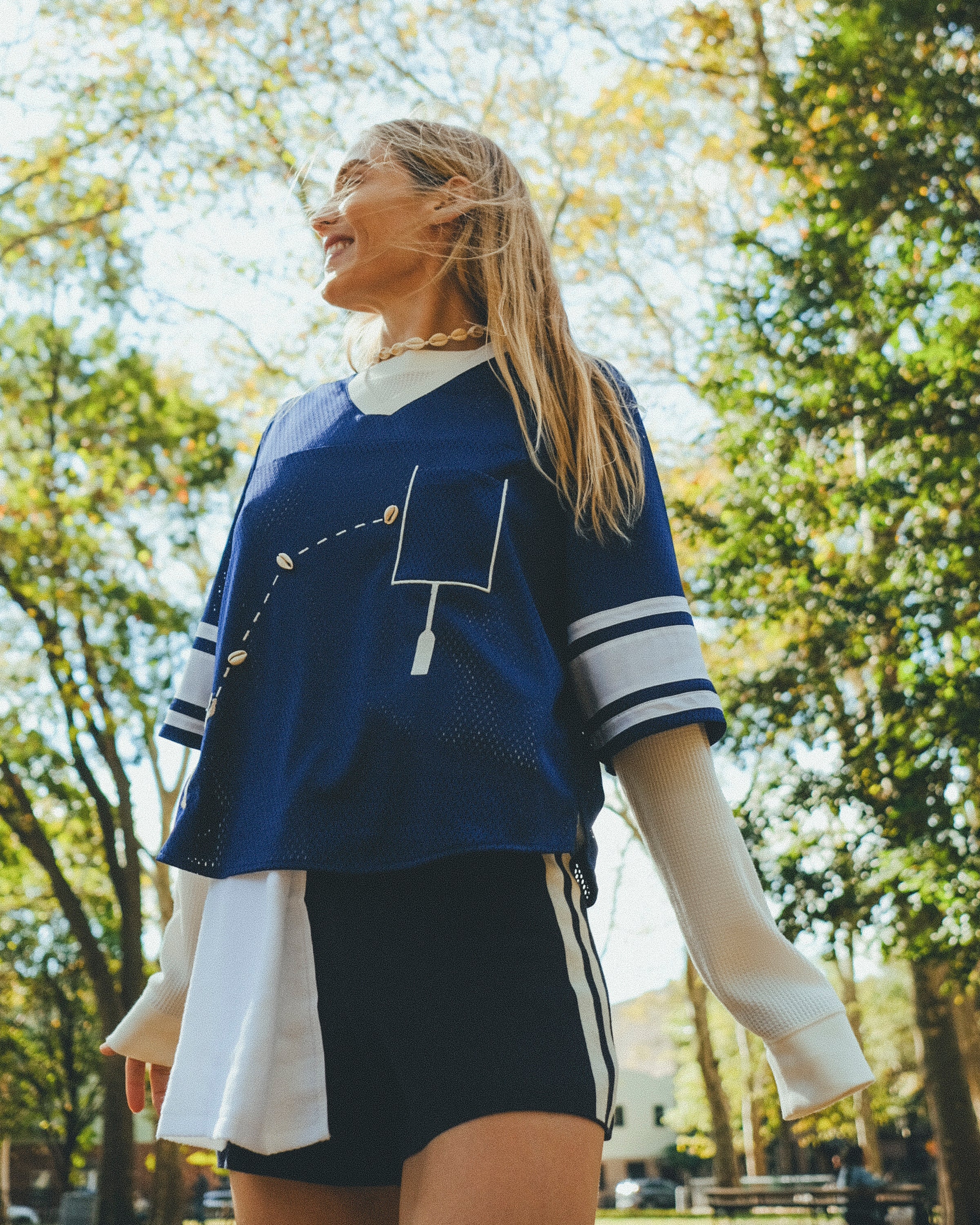Woman wearing blue football mesh jersey crop and smiling off to her right.