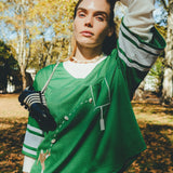 A woman wearing a green mesh football-style crop top with cowrie shells forming a football graphic, layered over a white long-sleeve shirt.