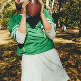 Woman in green mesh sports jersey and white shorts holding a football outdoors.