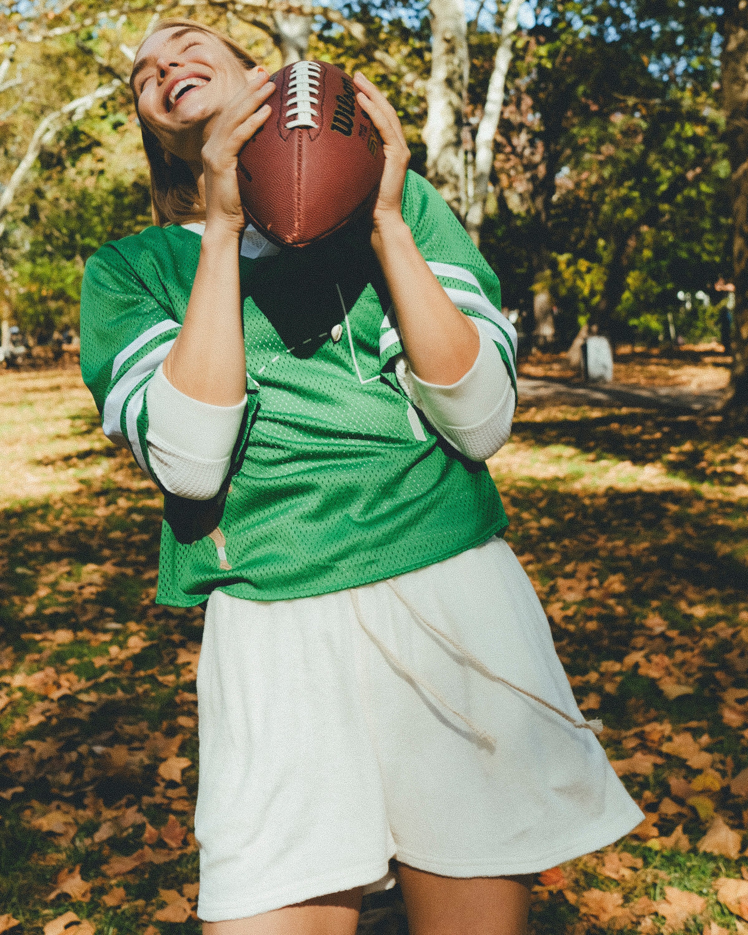 Woman in green mesh sports jersey and white shorts holding a football outdoors.