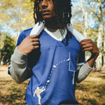 A man wearing the blue mesh football jersey, with a gray long sleeve layered underneath. He is carrying a towel around his neck. 