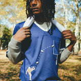 A man wearing the blue mesh football jersey, with a gray long sleeve layered underneath. He is carrying a towel around his neck. 