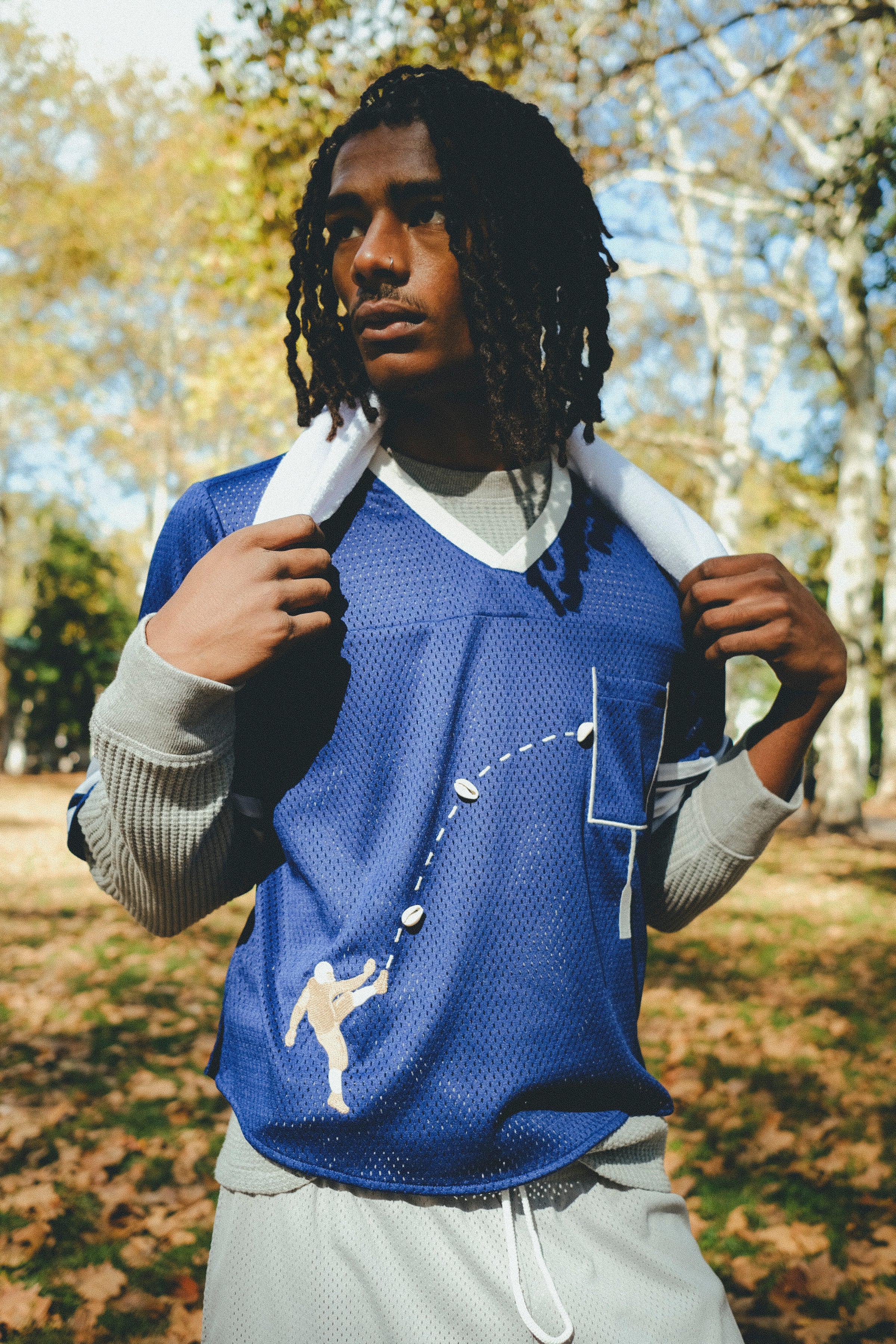 A man wearing the blue mesh football jersey, with a gray long sleeve layered underneath. He is carrying a towel around his neck. 