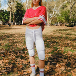 Woman wearing a red mesh football jersey and standing in a park.