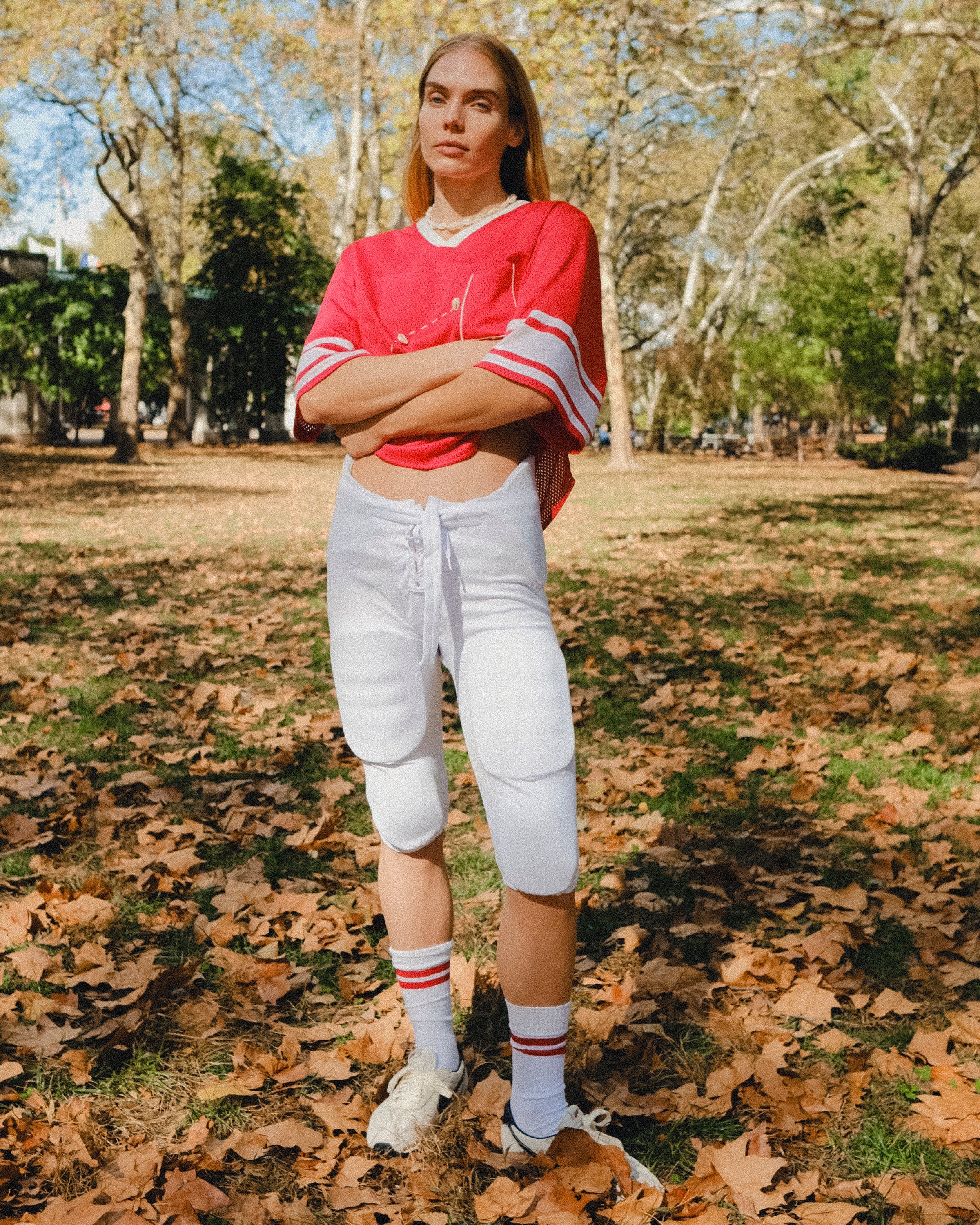 Woman wearing a red mesh football jersey and standing in a park.