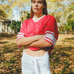 Woman wearing a red mesh football jersey and standing in a park.