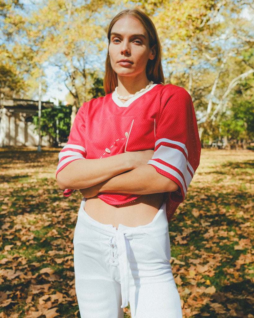 Woman wearing a red mesh football jersey and standing in a park.