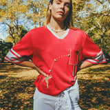 Woman wearing red mesh football cropped jersey with white football pants.