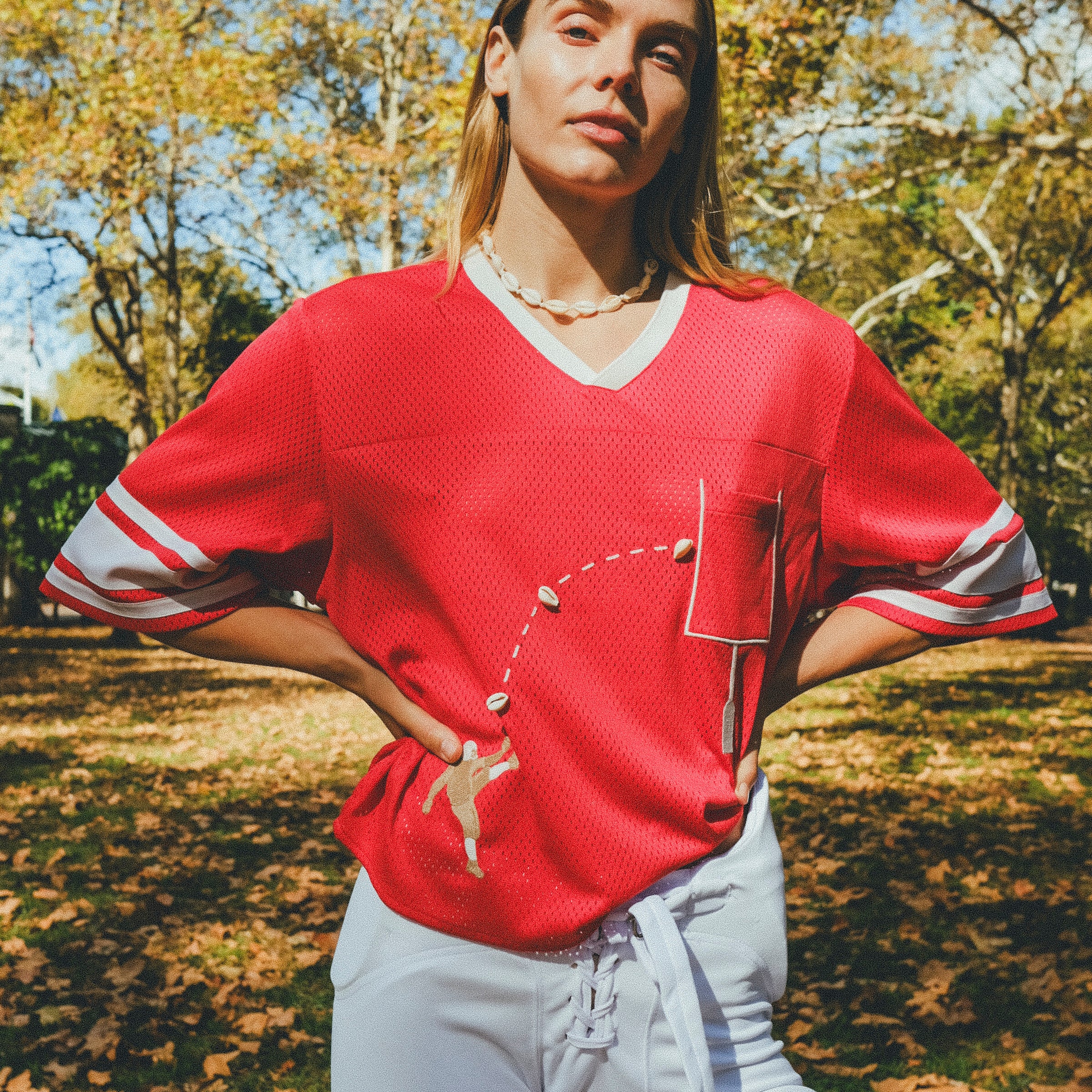 Woman wearing red mesh football cropped jersey with white football pants.