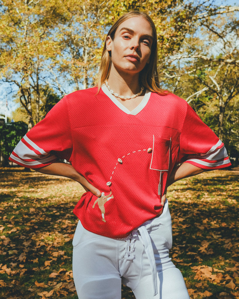 Woman wearing red mesh football cropped jersey with white football pants.