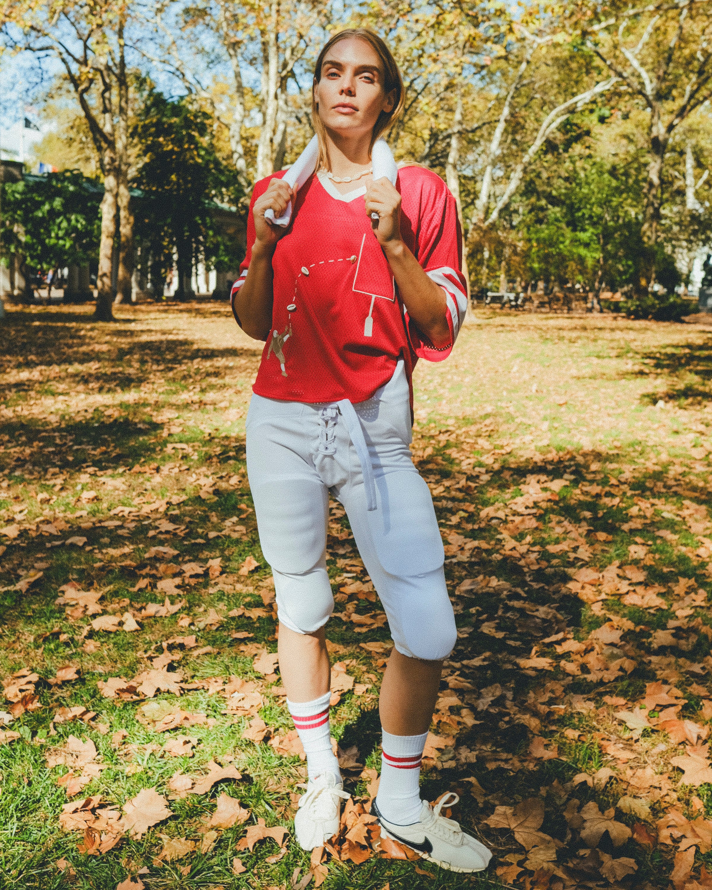 Woman wearing a red mesh football jersey and standing in a park.