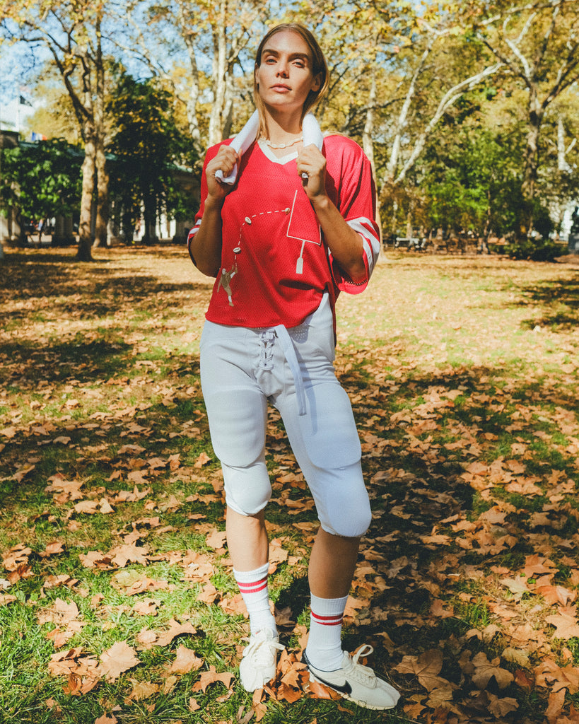Woman wearing a red mesh football jersey and standing in a park.