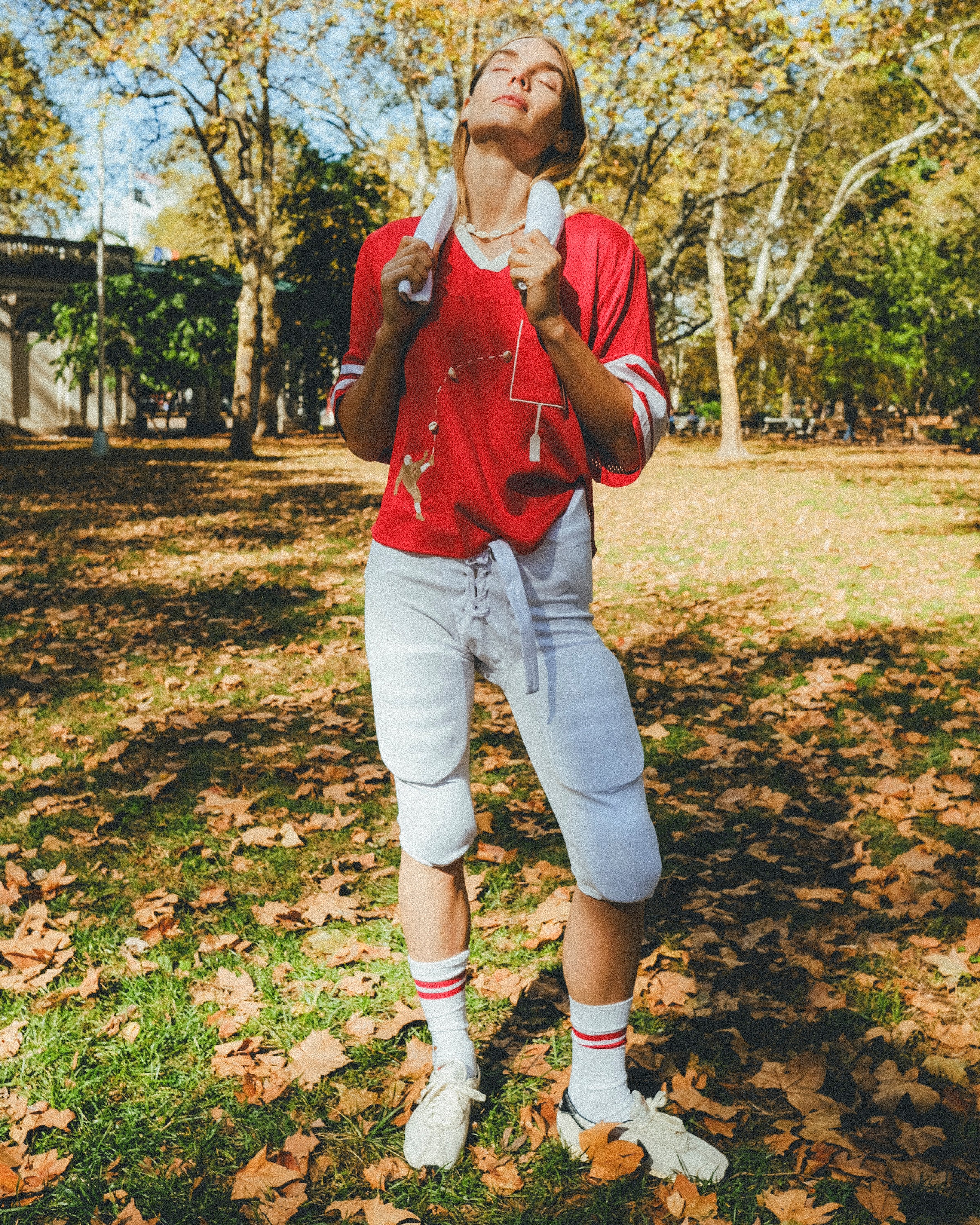 Woman wearing a red mesh football jersey and standing in a park, wearing a towel around her neck.