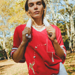 Woman wearing a red mesh football jersey and standing in a park, wearing a towel around her neck.
