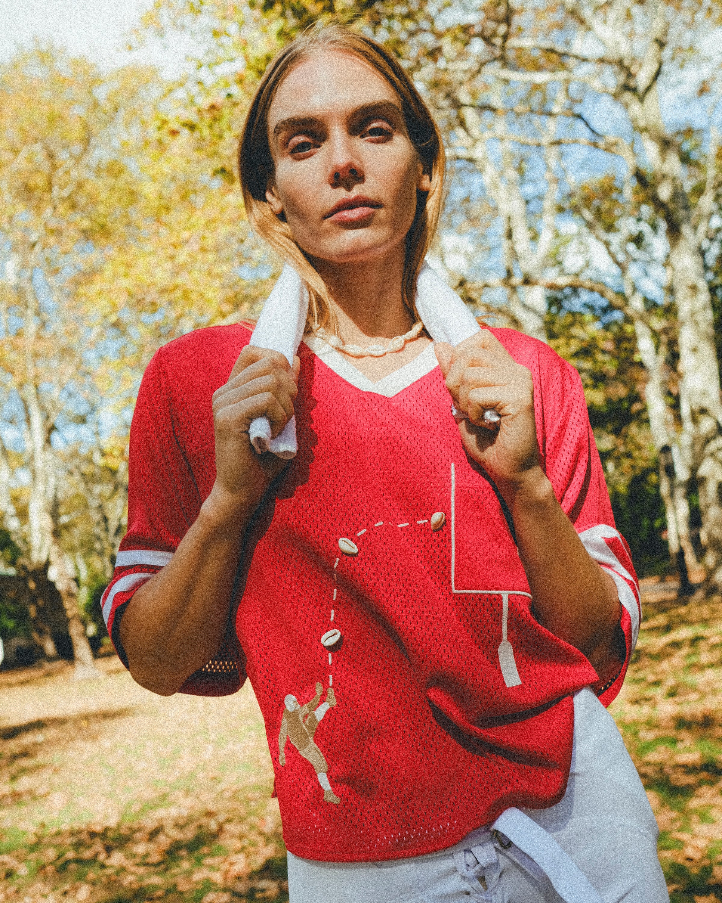 Woman wearing a red mesh football jersey and standing in a park, wearing a towel around her neck.