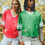 Two people wearing red and green sports jerseys and standing outdoors.