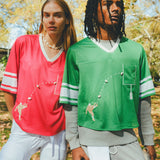 Two people wearing red and green sports jerseys and standing outdoors.