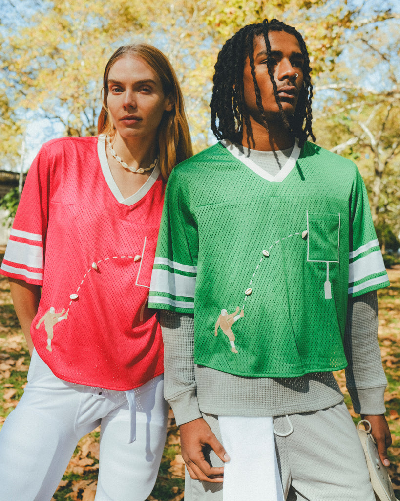 Two people wearing red and green sports jerseys and standing outdoors.