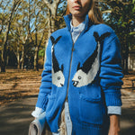 Female model wearing a blue cardigan with fish patterns in a park setting.