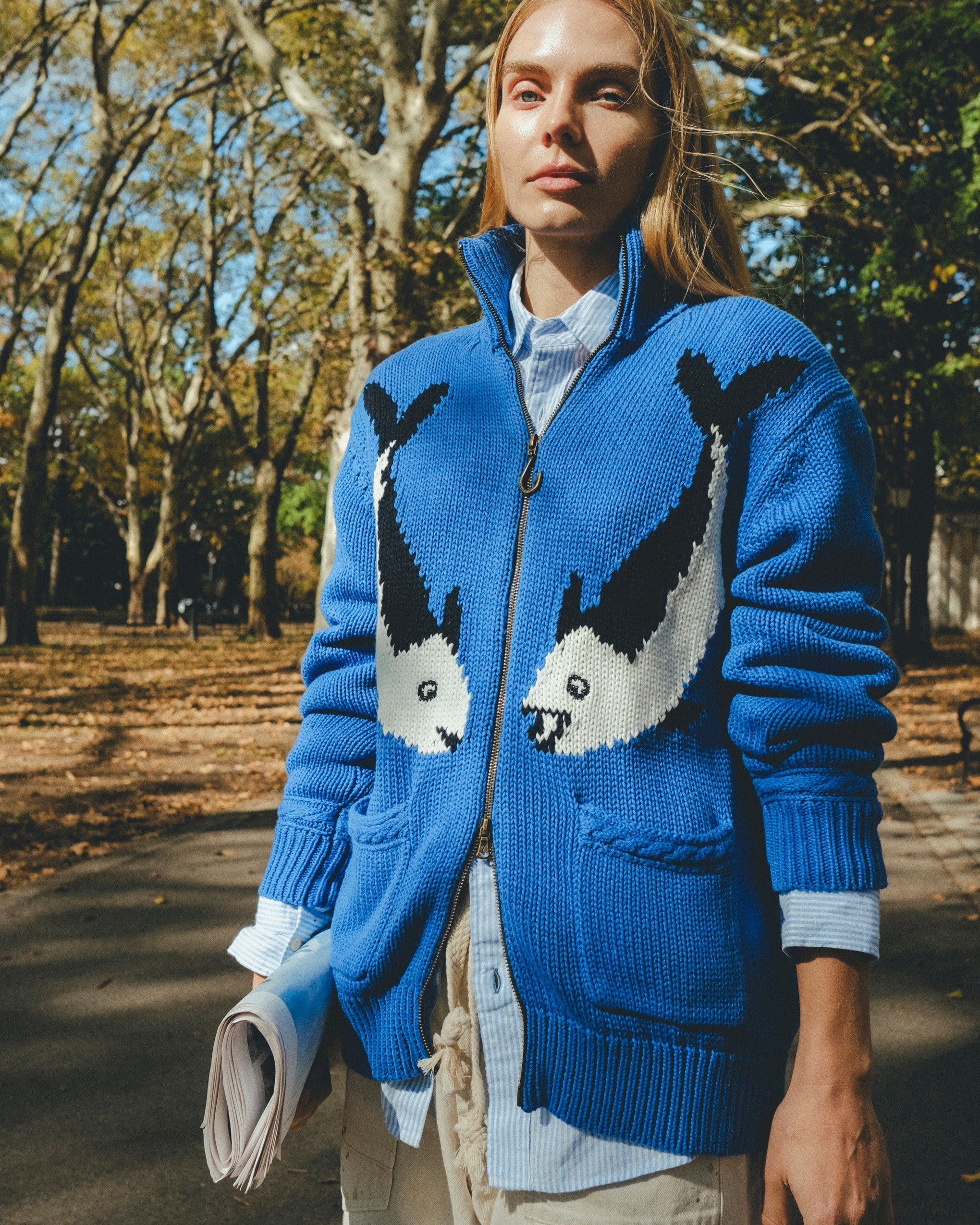 Female model wearing a blue cardigan with fish patterns in a park setting.