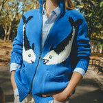 Blue zip-front knit sweater with mirrored fish motifs, styled outdoors.
