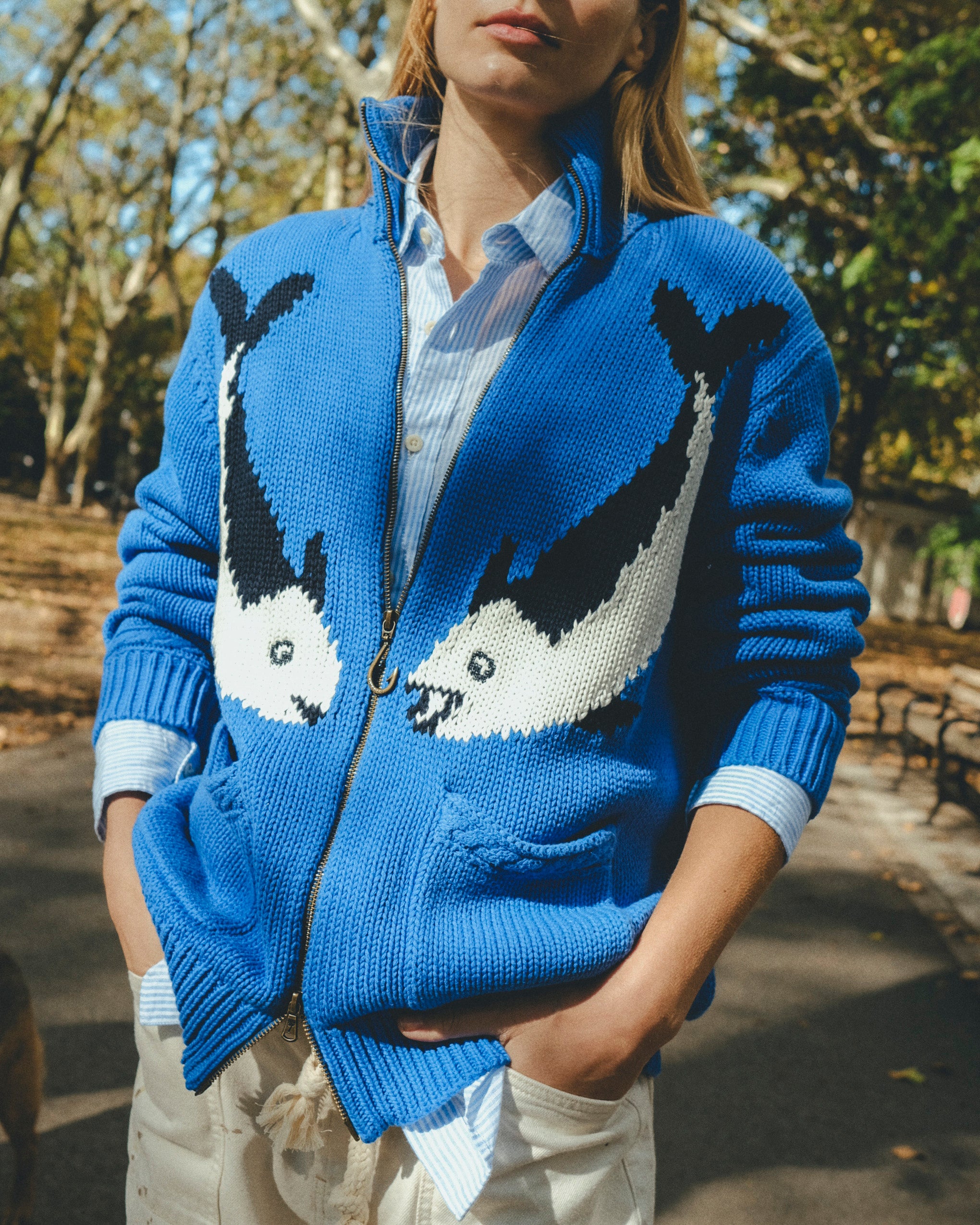 Blue zip-front knit sweater with mirrored fish motifs, styled outdoors.
