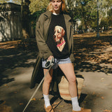 Woman wearing a black knit sweater with an intarsia dog portrait on the front and a red collar detail.