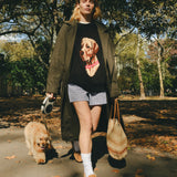 Woman wearing a black knit sweater with an intarsia dog portrait on the front and a red collar detail, walking a dog through the park.