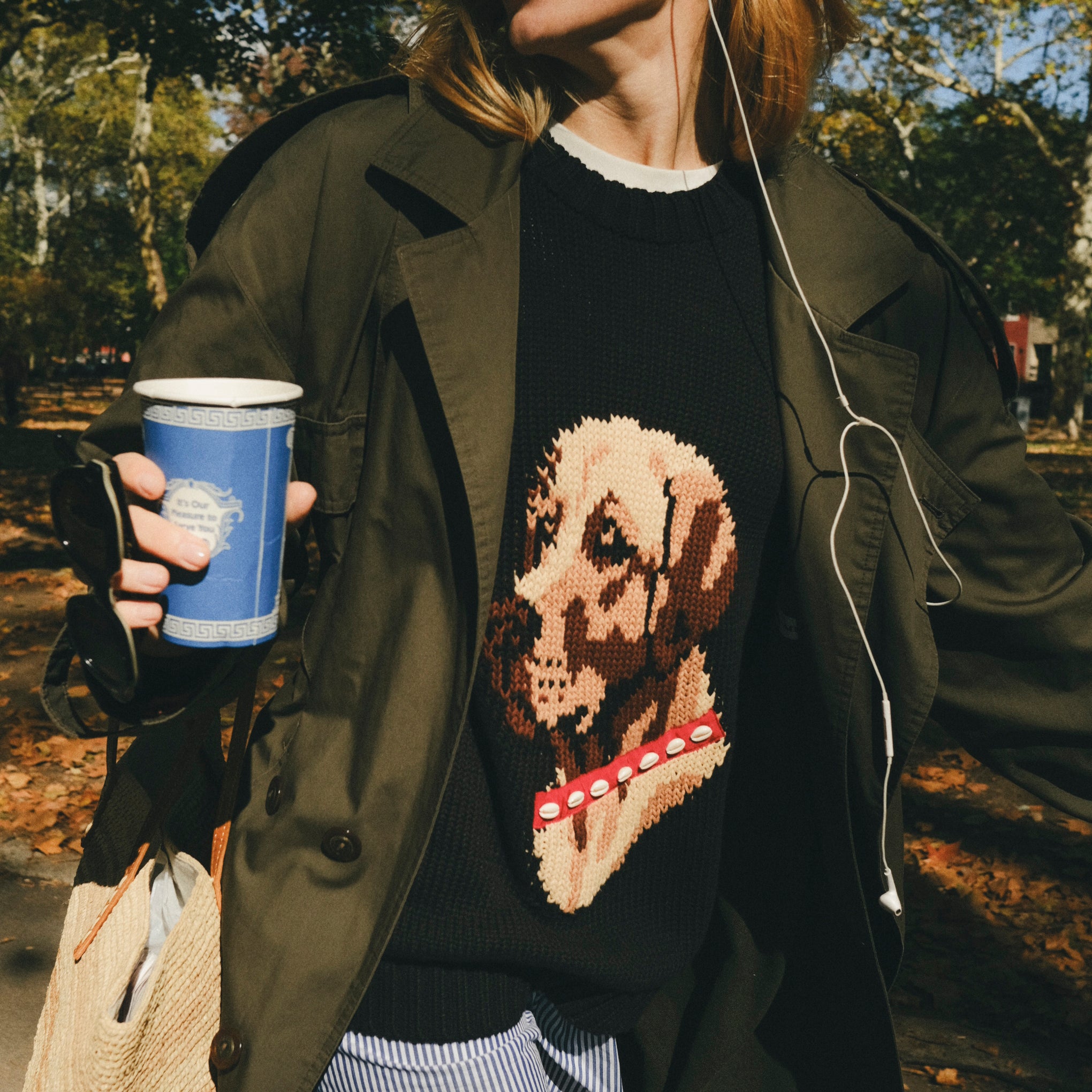 Woman wearing a black knit sweater with ribbed collar, cuffs, and hem, featuring an intarsia dog portrait on the front wearing a red collar with white shell details.
