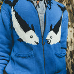 Close-up of a blue zip-up knit sweater featuring two fish and a fish hook zipper pull.
