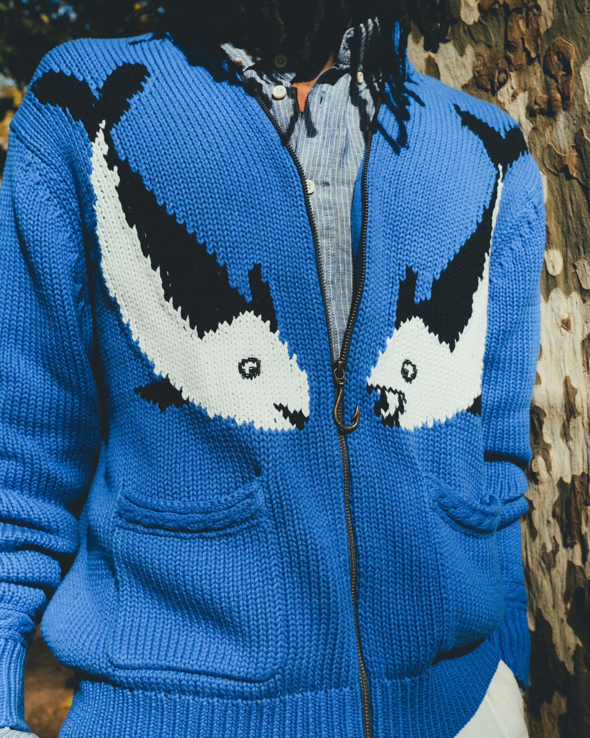 Close-up of a blue zip-up knit sweater featuring two fish and a fish hook zipper pull.