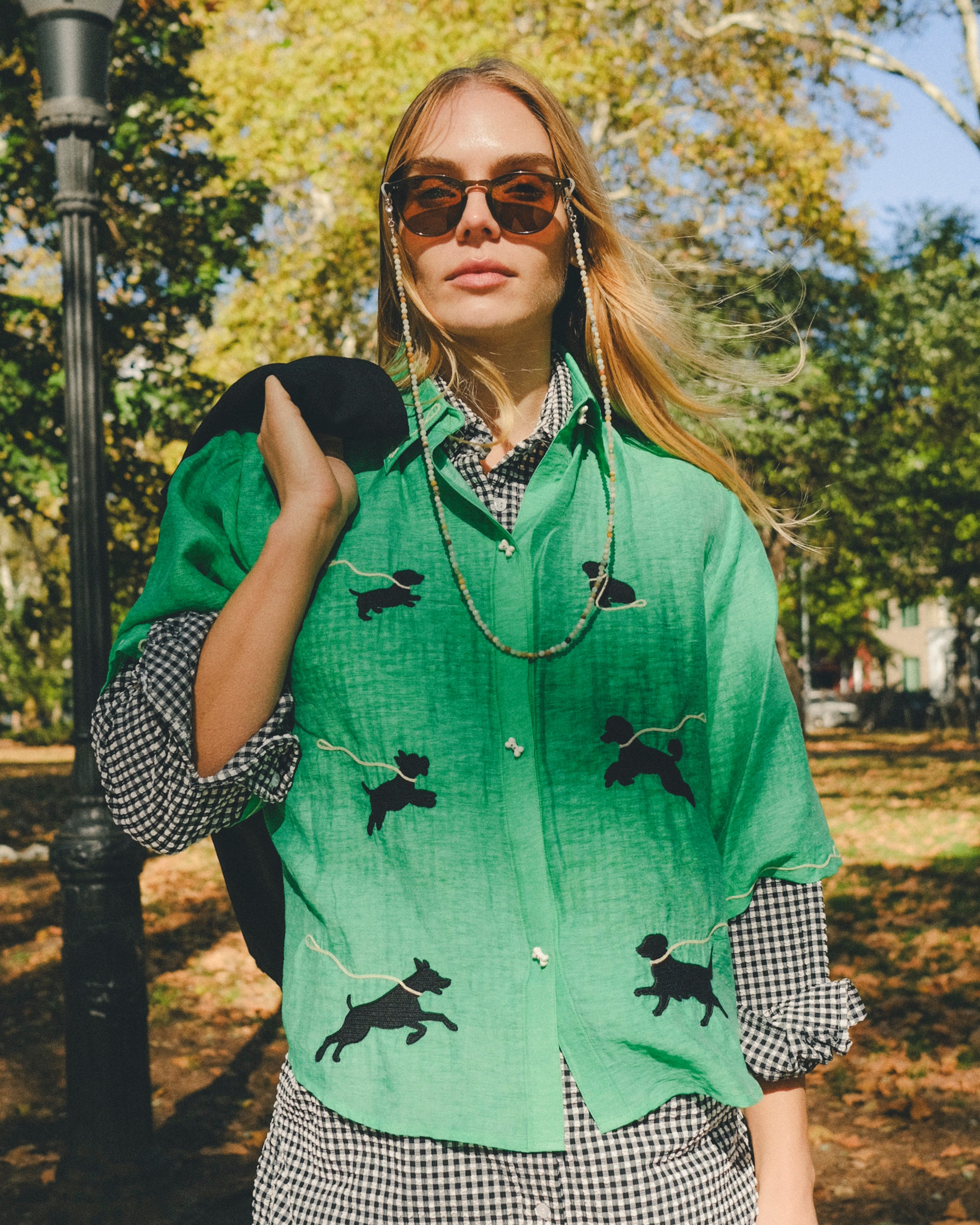 Woman wearing a green cropped cabana shirt with black dog silhouettes and white leash embroidery, layered over a black-and-white gingham shirt.
