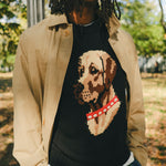 Man wearing a black knit sweater with an intarsia dog portrait on the front and a red collar detail.