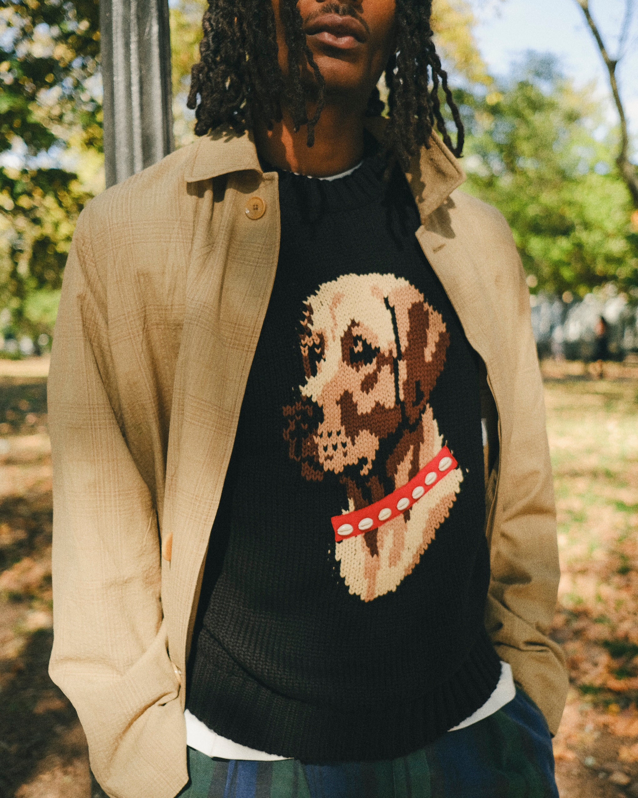 Man wearing a black knit sweater with an intarsia dog portrait on the front and a red collar detail.
