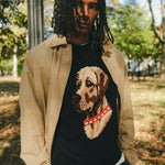 Man wearing a black knit sweater with ribbed collar, cuffs, and hem, featuring an intarsia dog portrait on the front wearing a red collar with white shell details.