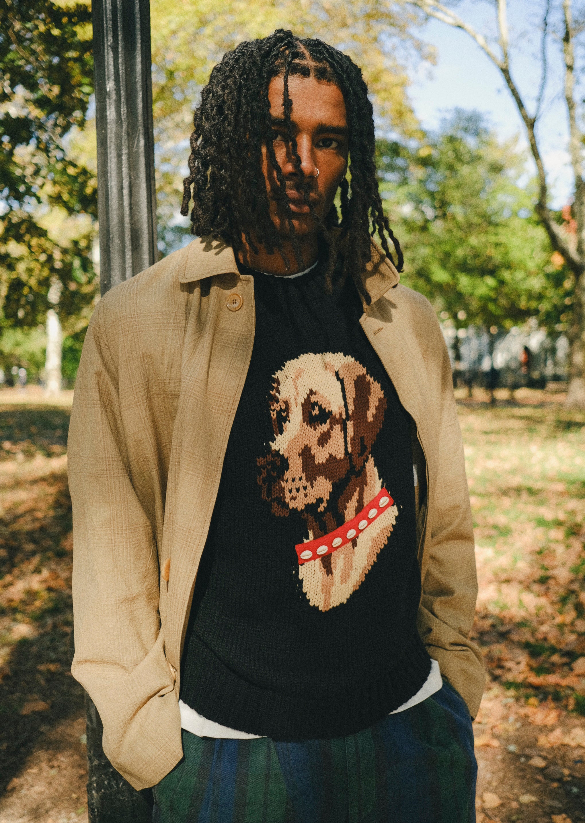 Man wearing a black knit sweater with ribbed collar, cuffs, and hem, featuring an intarsia dog portrait on the front wearing a red collar with white shell details.