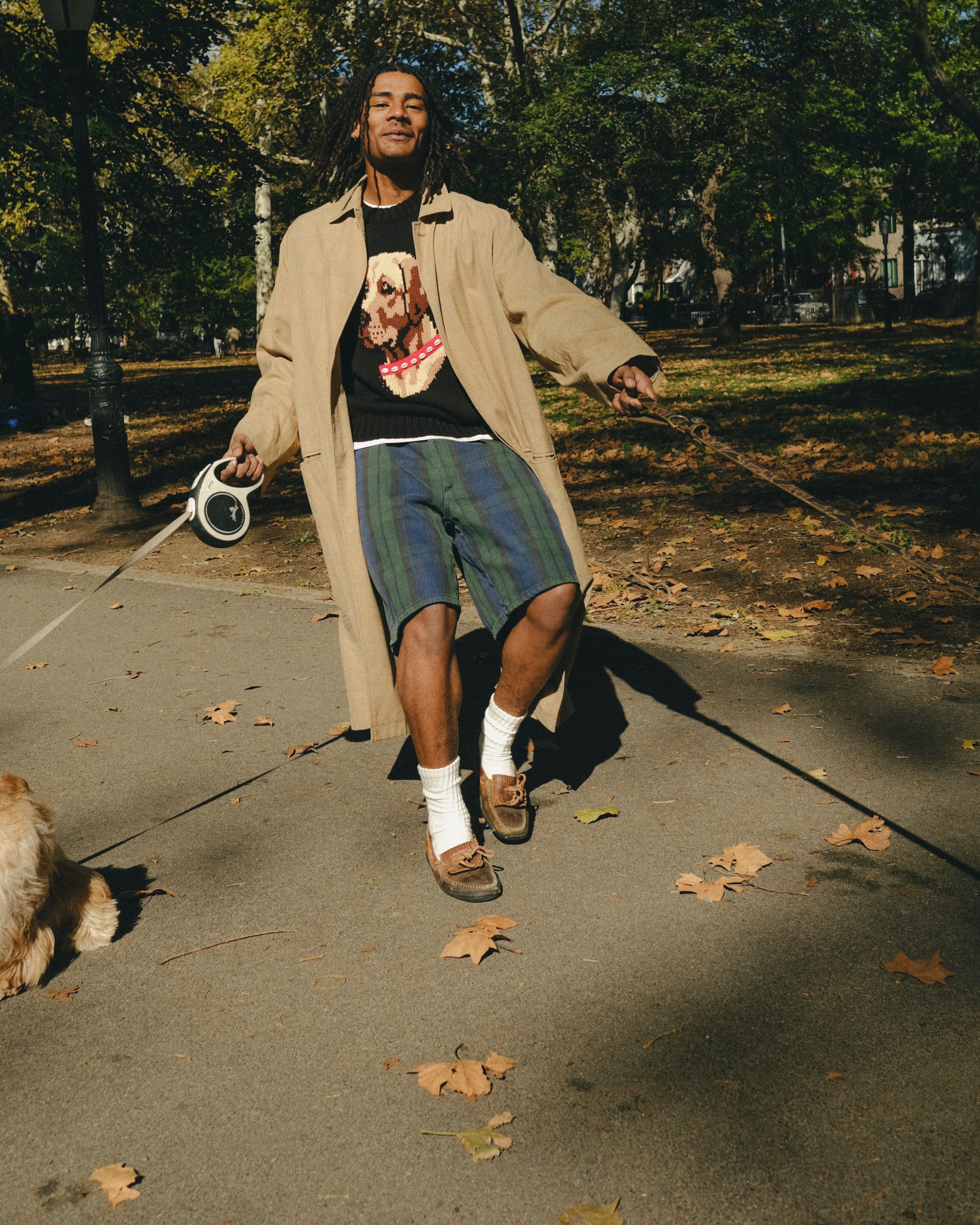 Man wearing a black knit sweater with an intarsia dog portrait on the front and a red collar detail while walking a dog.