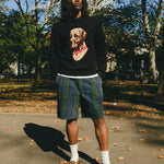 Man wearing a black knit sweater with an intarsia dog portrait on the front and a red collar detail.