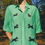 Close-up of a green cropped cabana shirt with black dog silhouettes and white leash embroidery, finished with dog bone–shaped buttons.