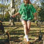 Woman wearing a green cropped cabana shirt with black dog silhouettes and white leash embroidery across the front.