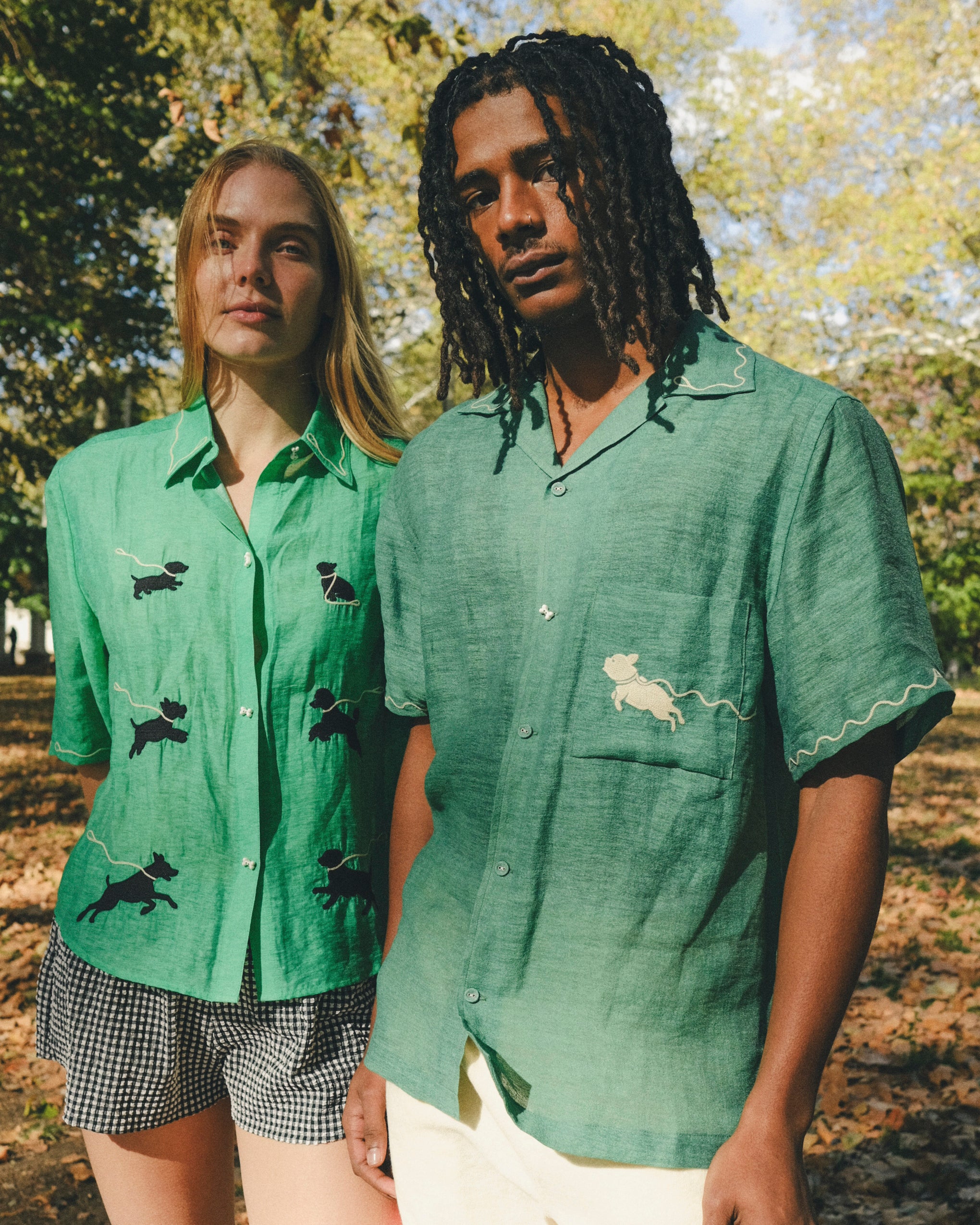 Two models wearing green cabana shirts with embroidered dog graphics, contrast wavy piping, and dog bone button detail at the center front.