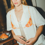 Woman wearing a white embroidered shirt  with a plate of croissants on a wooden table next to her. 